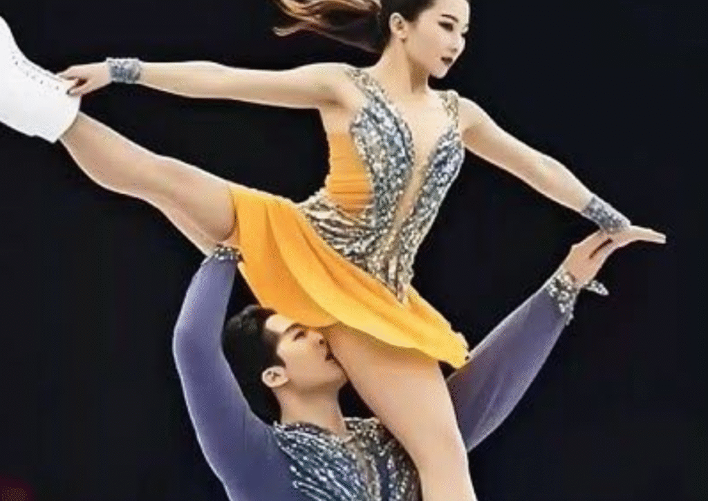 figure skating pair performing dramatic lift with female skater in yellow costume