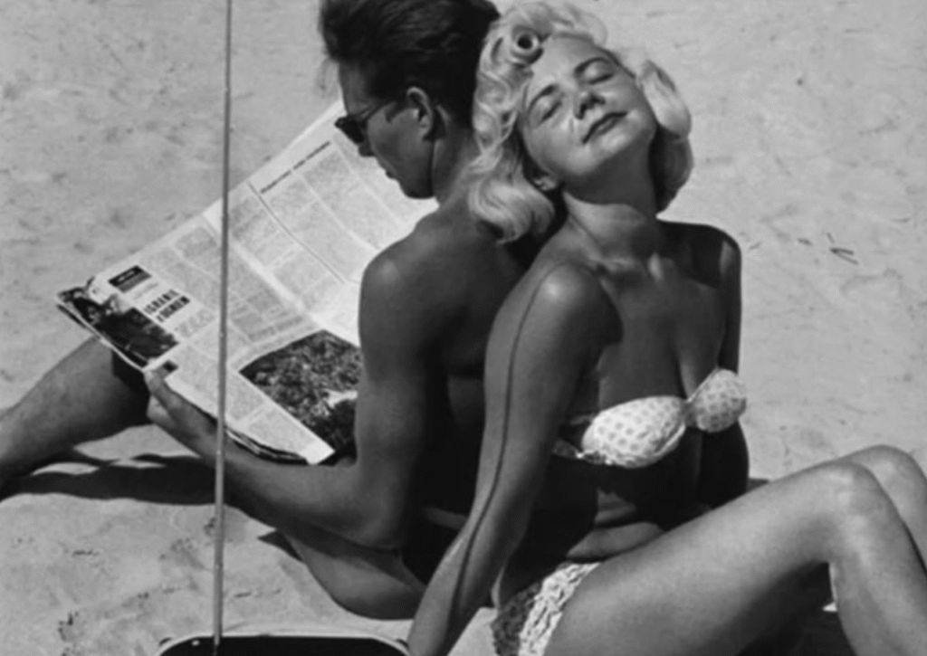 Woman sunbathing while man reads at the beach