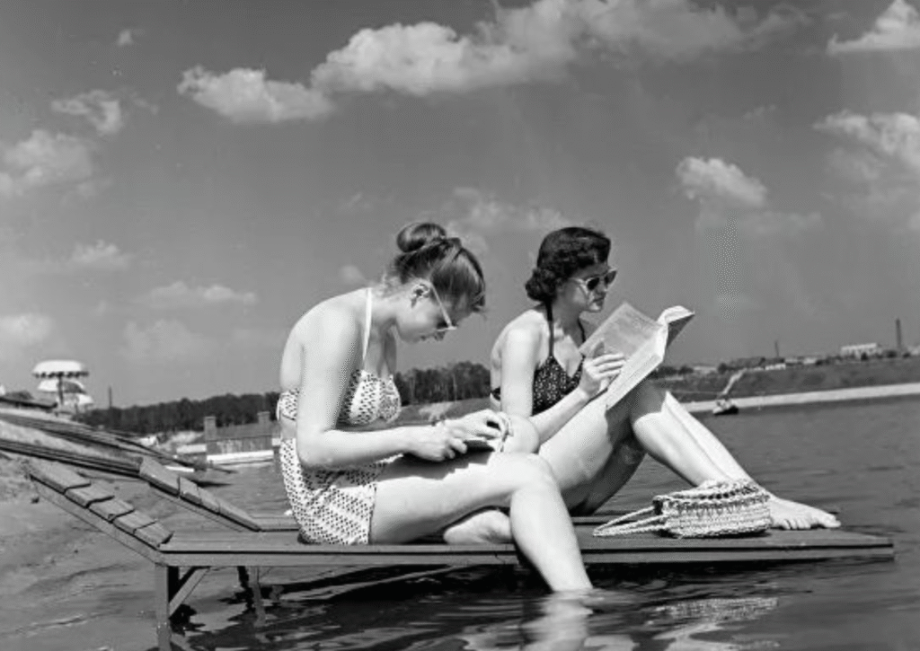 Women reading in swimsuits by the river dock