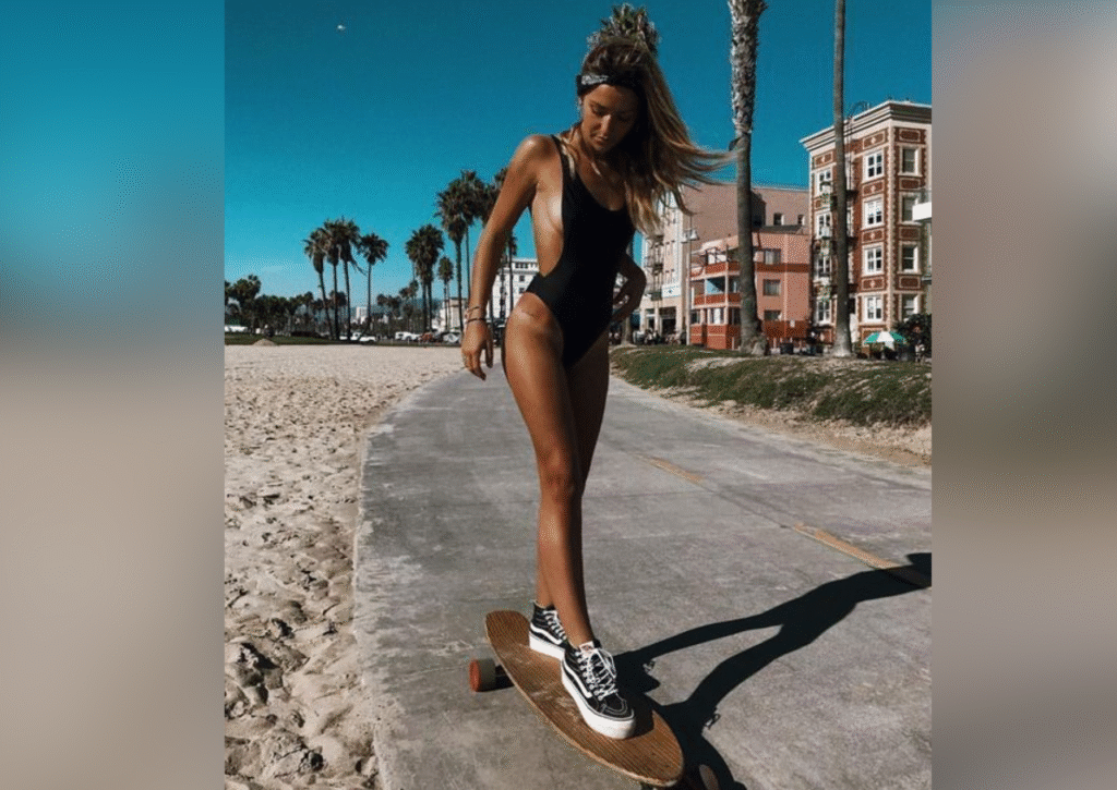 Woman riding longboard on beach in one-piece swimsuit