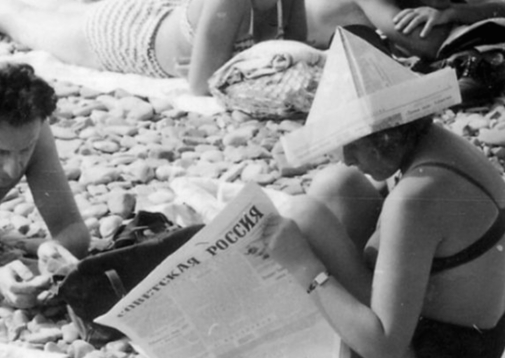 Woman wearing newspaper hat while reading at pebble beach